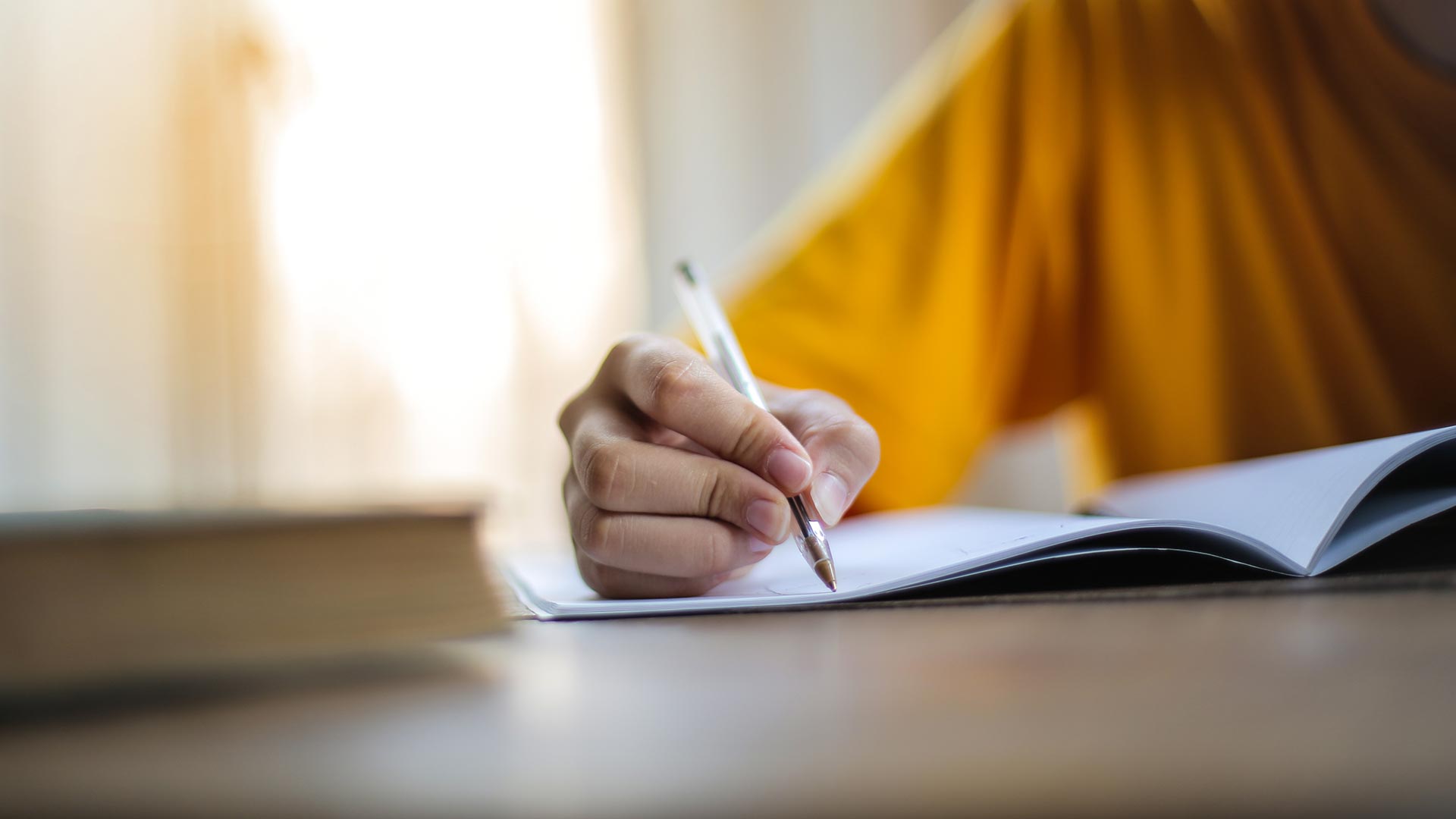 someone in a yellow shirt handwriting on paper