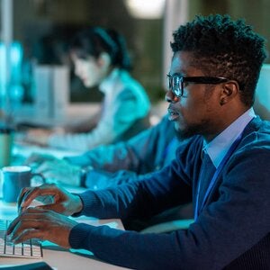 person-in-front-of computer-with-another-person-in-background-on-computer