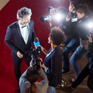 Reporter interviewing celebrity while being photographed by paparazzi photographers at red carpet event