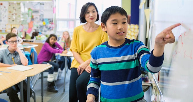 Young student pointing to the white board in a classroom