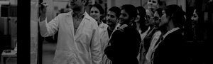 group of students in a robotics lab watching an instructor write at a white board