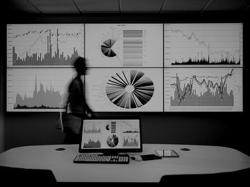 A man in front of a large screen with data and charts on it.