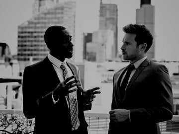 Businessman discussing with his business partner, standing outdoor with city scape in the background.