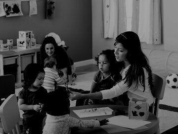 teacher with a child on her lap passing crayons to another child