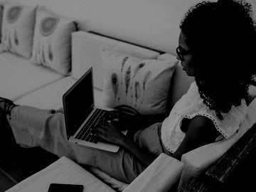 Woman working from home sitting on patio furniture while writing on her laptop