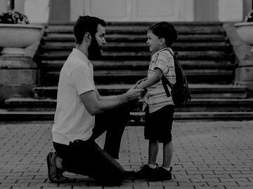 a dad kneeling down to talk eye to eye with his young son