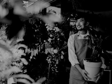 Asian male florist, holding potted plant outside his workplace. 