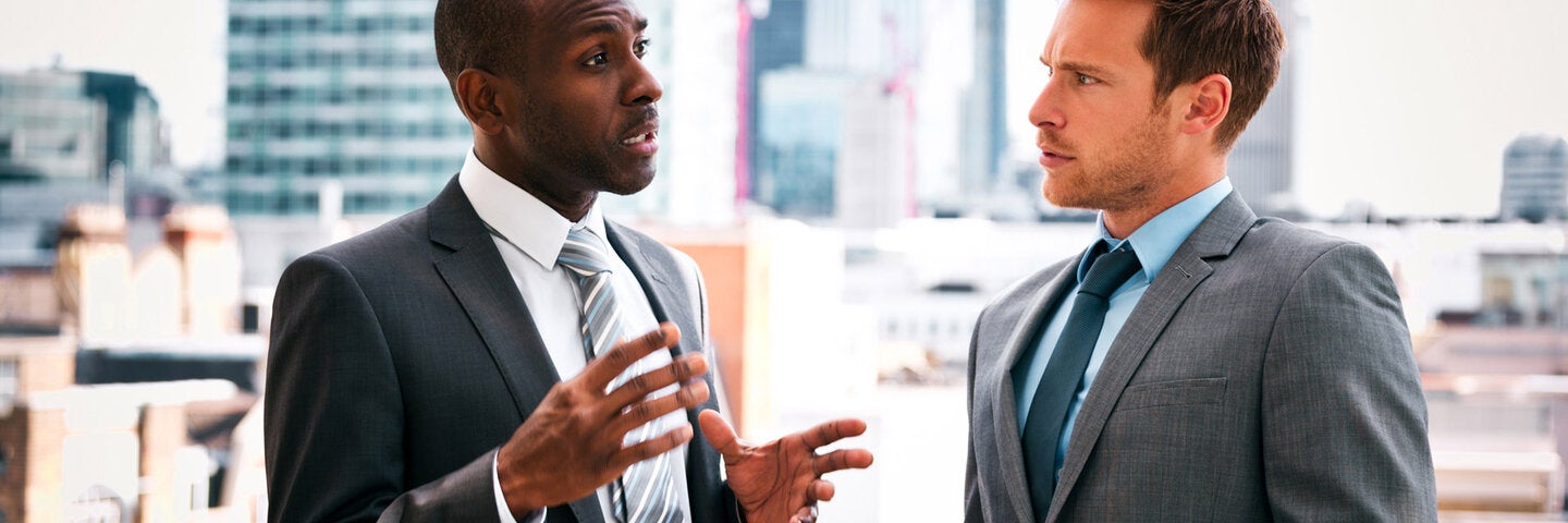 Businessman discussing with his business partner, standing outdoor with city scape in the background.