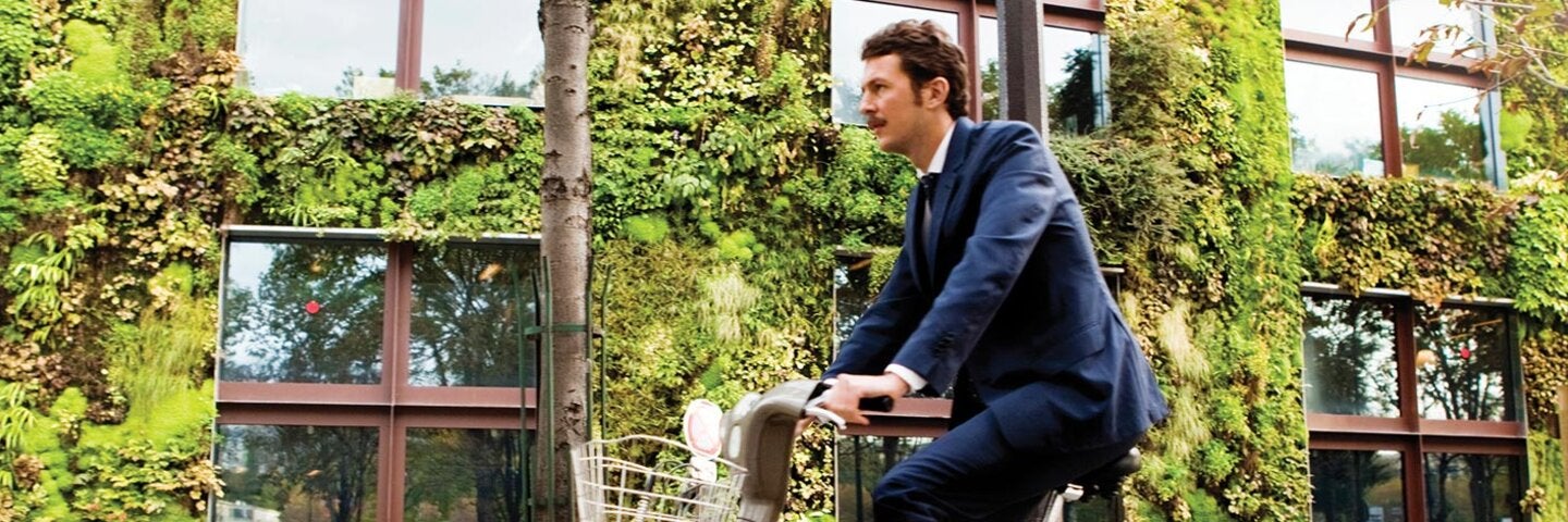 Businessman riding a bike through a green business complex.