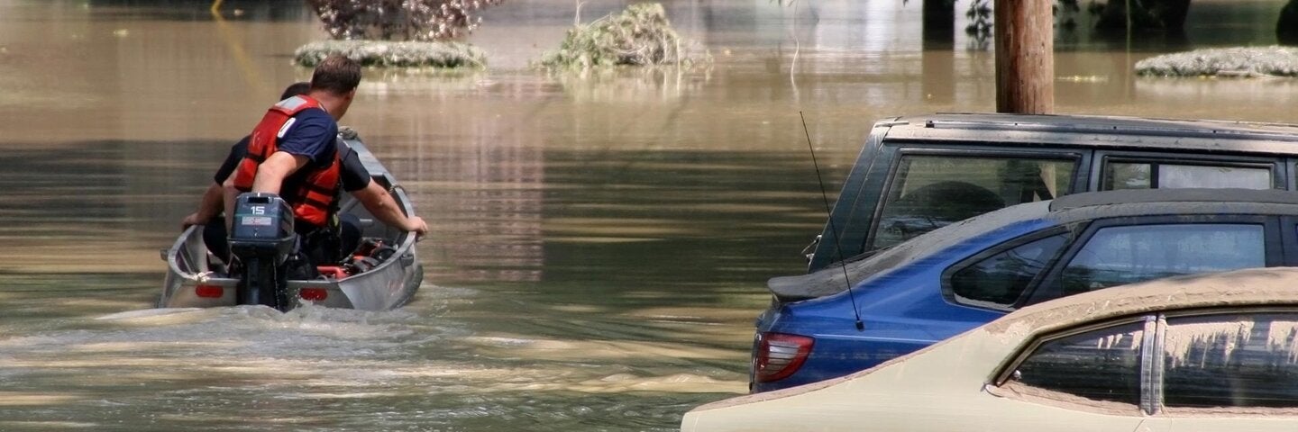 small motor boat going down a flooded street next to parked cars