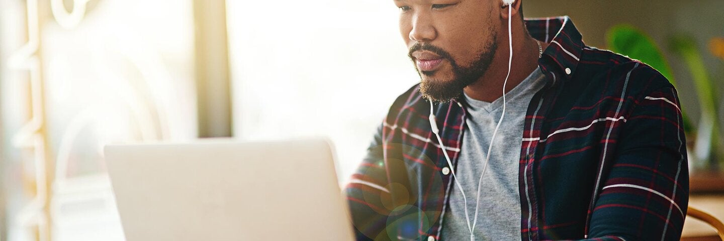 man wearing earbuds sitting at a laptop with a coffee