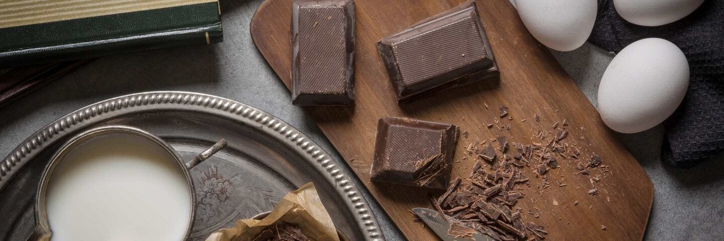 Chocolate, eggs, milk, and knife on kitchen counter and cutting board.