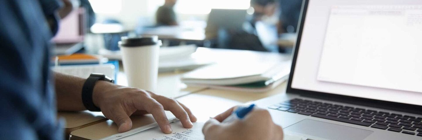 Male adult student doing assignment at laptop in classroom