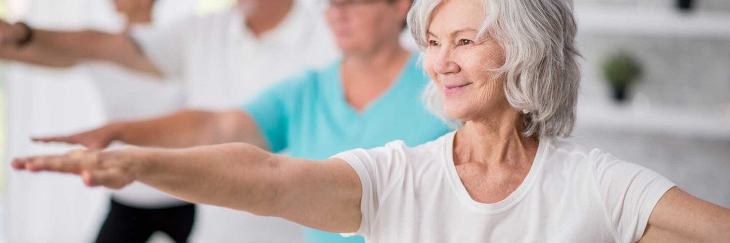 A senior woman is smiling while stretching out her arms.