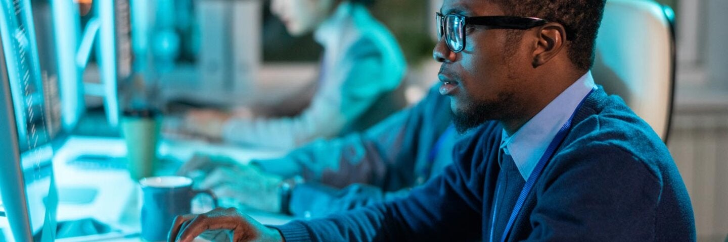 person in front of a computer with another person in the background on a computer