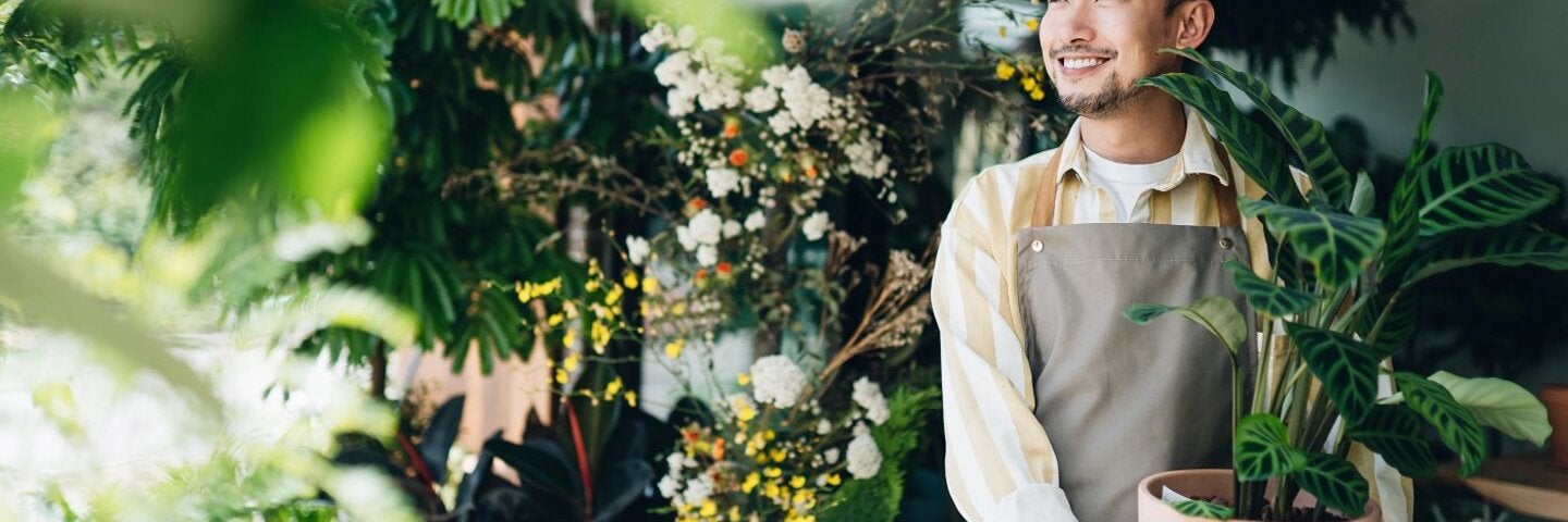 Asian male florist, holding potted plant outside his workplace. 